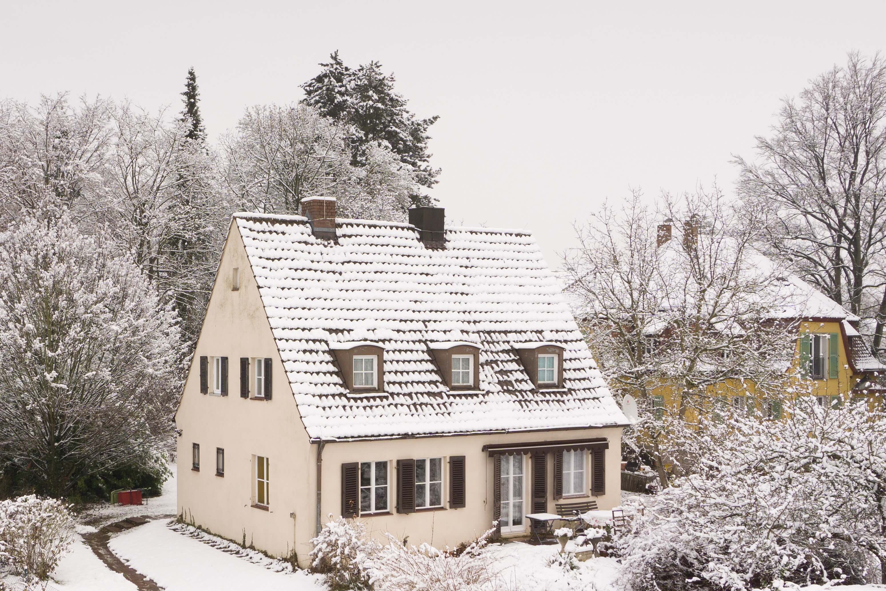 Een huis in de winter, met sneeuw op het dak en in de tuin.