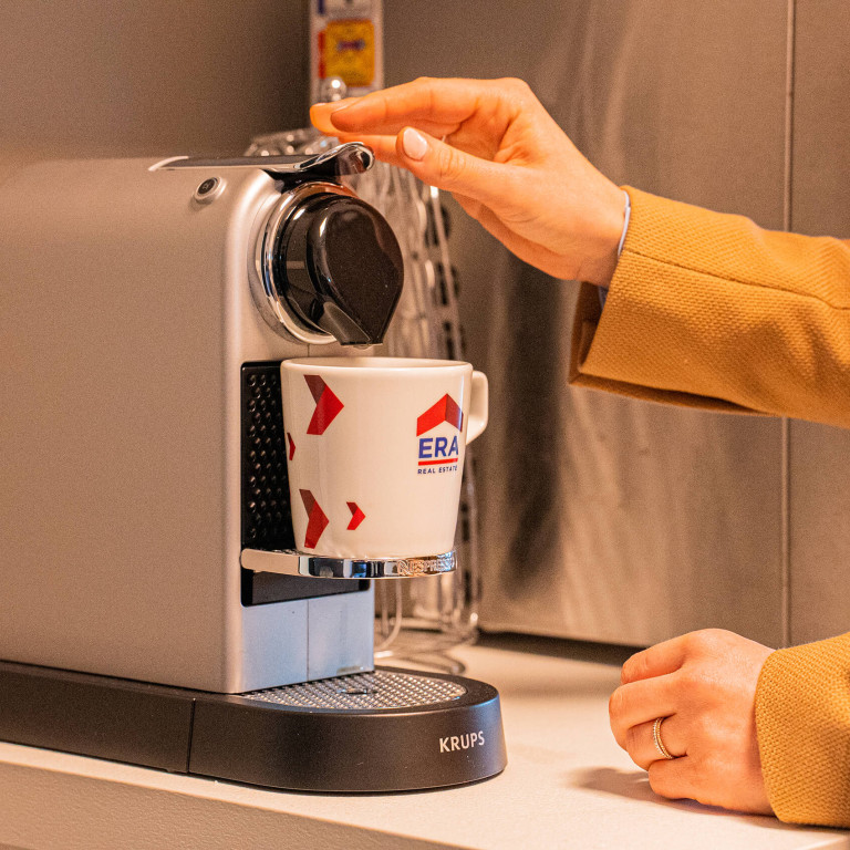 Een vrouw zet een koffie in een ERA koffietas.