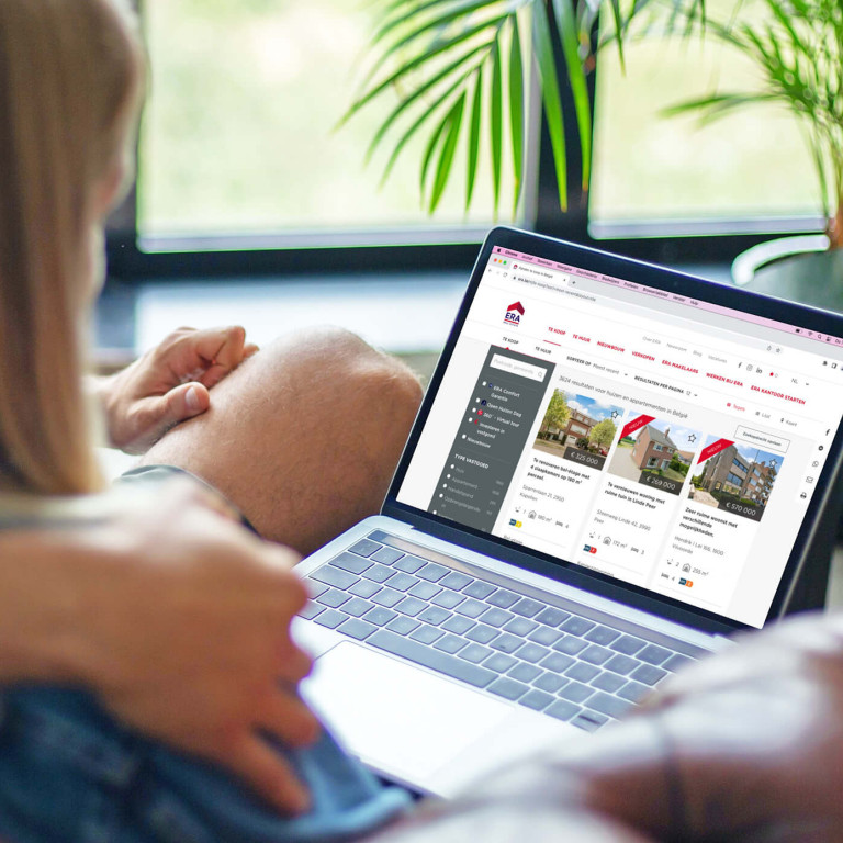 Een koppel zit samen in de zetel en bekijken de ERA immowebsite op een laptop.
