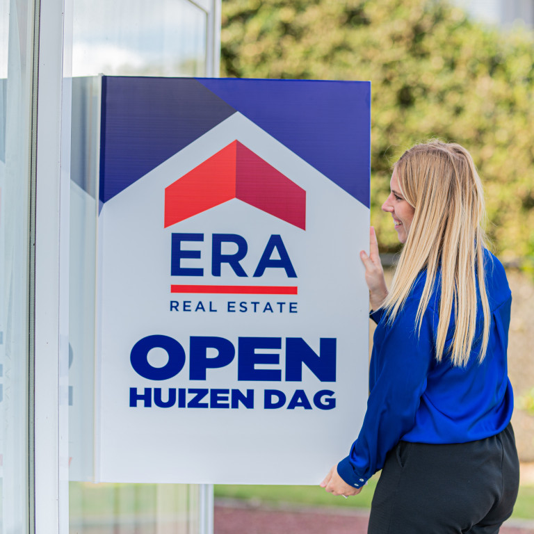 Een ERA makelaar hangt een ERA Open Huizen Dag V-Bord op.