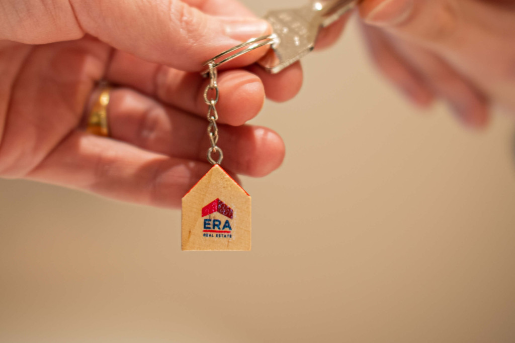 Een persoon geeft een sleutel met een ERA sleutelhanger door aan iemand anders.