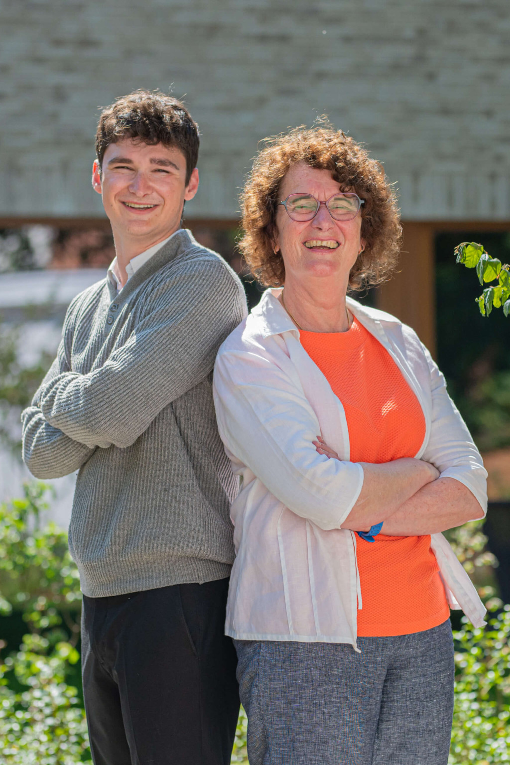 Topmakelaars Dorine en Matthew lachen naar de camera terwijl ze rug tegen rug in de zon staan.