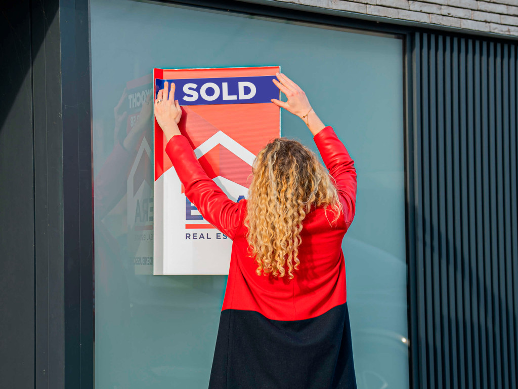 An ERA broker puts a sticker, with the word sold on it, on a sale sign.
