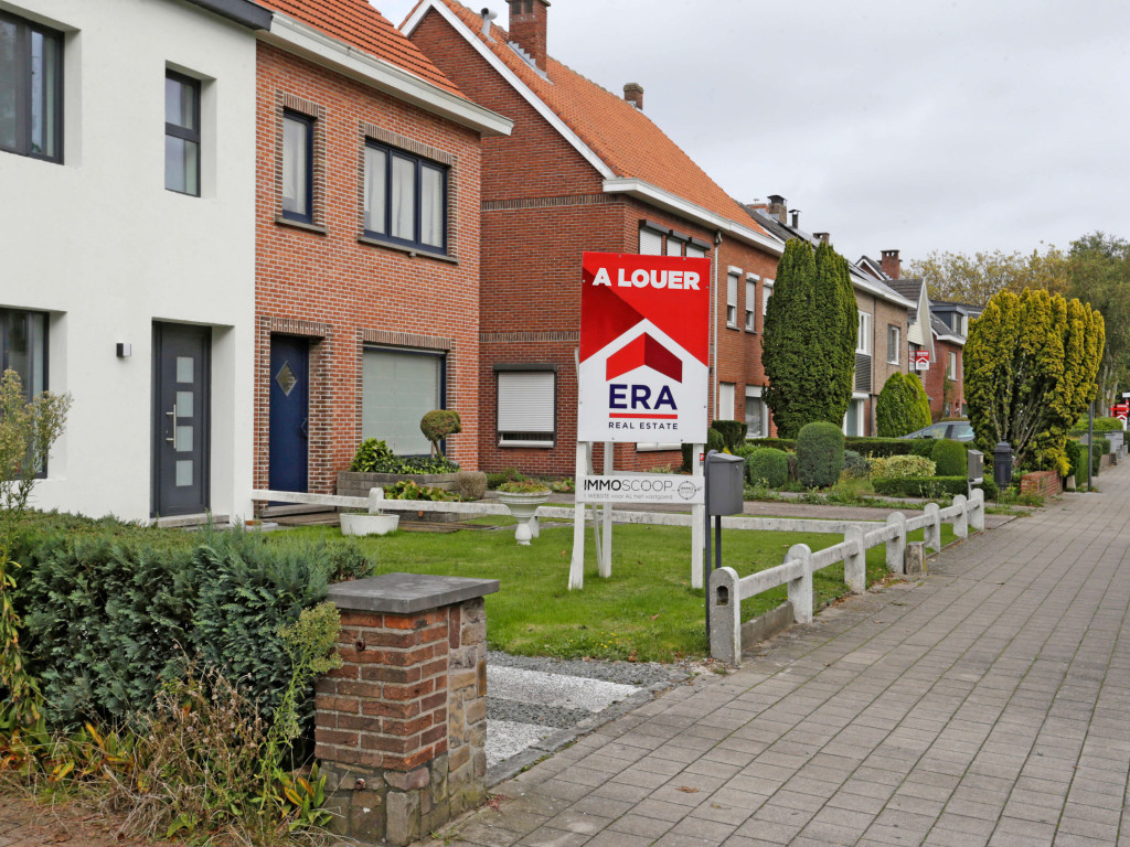 Il y a un grand panneau en V rouge dans le jardin avant d'une maison qui est mise en vente par ERA.